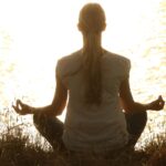 Woman meditating at sunset representing neurowellness and mind-body balance
