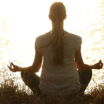 Woman meditating at sunset representing neurowellness and mind-body balance